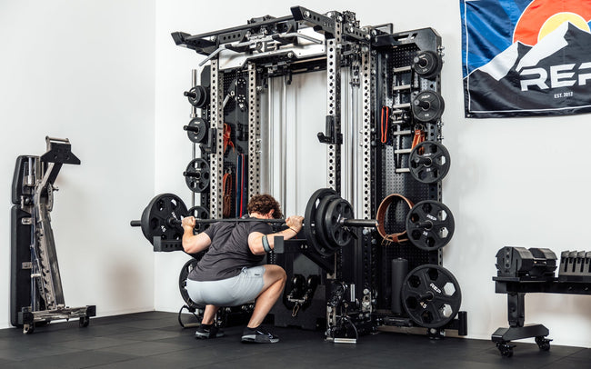 An athlete performing barbell squats off the front of the Wall-Mounted Ares™ 2.0 with spotter arms